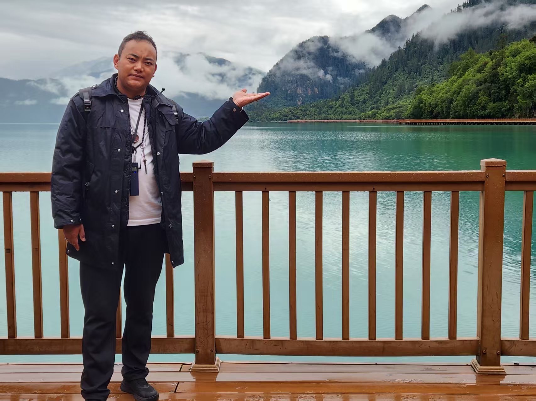 Jimmy gesturing towards a misty lake and mountains
